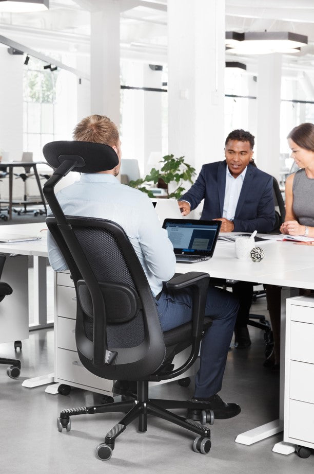 People working at a desk in an office setting with a black office chair.