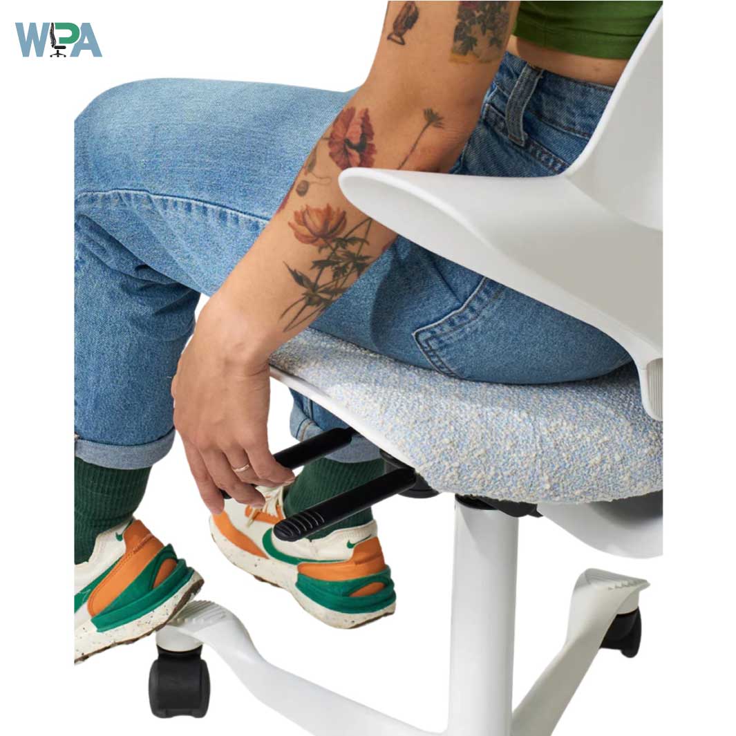 Person sitting on a white office chair with a tattooed arm, wearing blue jeans and colorful sneakers.