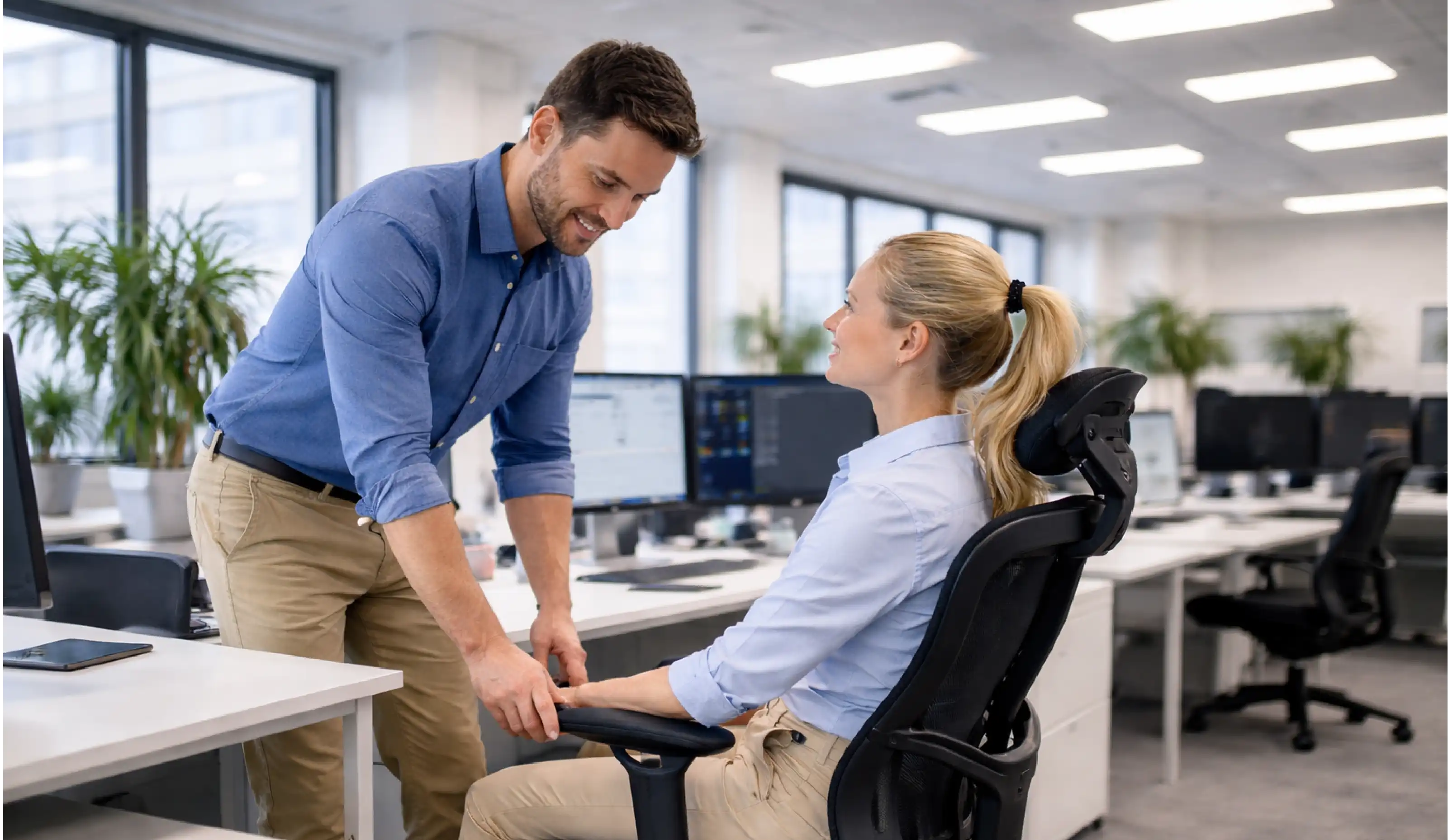 Man adjusting a woman's chair in an office setting